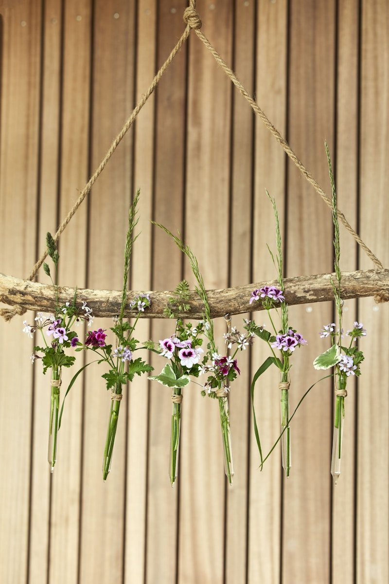 Flowers hang in glass tubes from a wood branch.