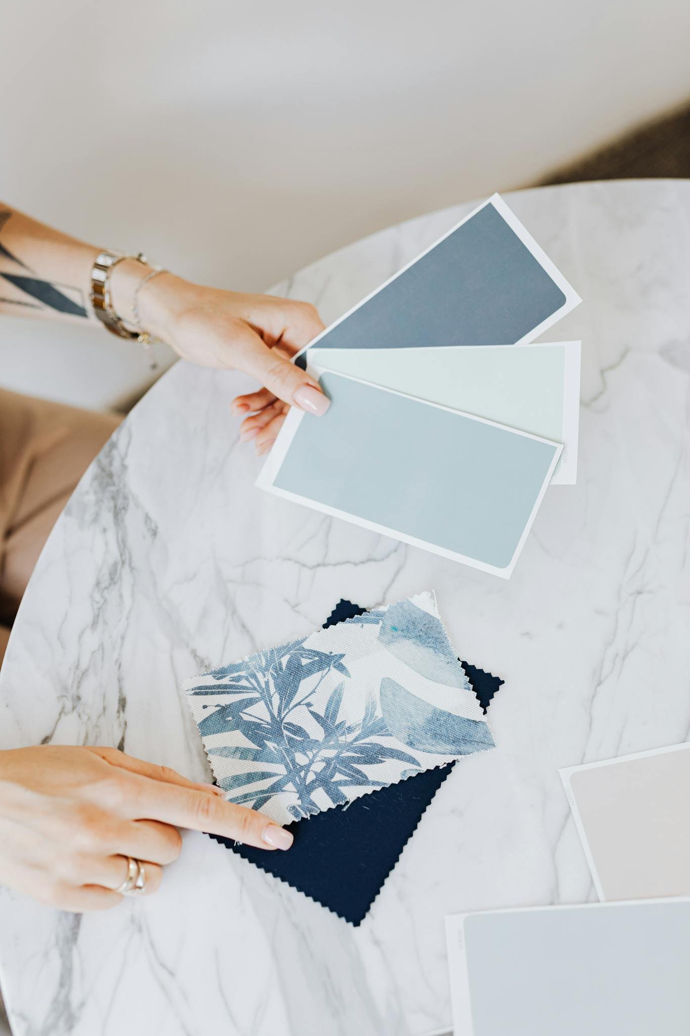 A woman holding and selecting blue color swatches on a marble table, focusing on interior design choices.
