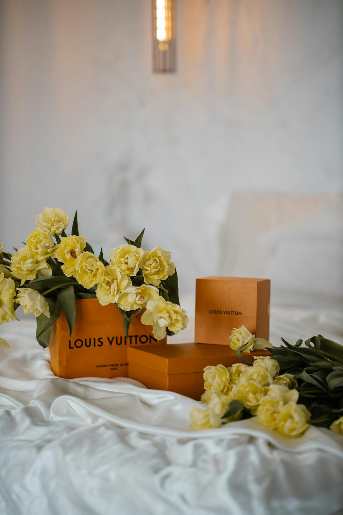 Yellow tulips elegantly draped over luxury boxes on a satin bedspread, creating a serene and classy ambiance.